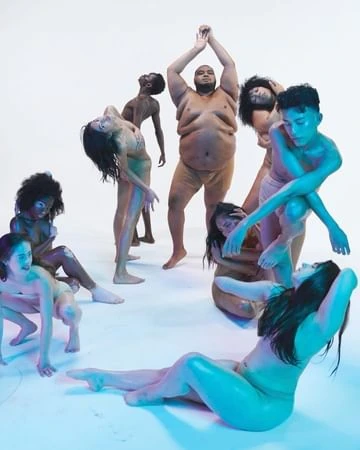 A group of nine diverse adults pose in a semi-circle against a white backdrop, creating a visually striking composition with neutral skin tones.