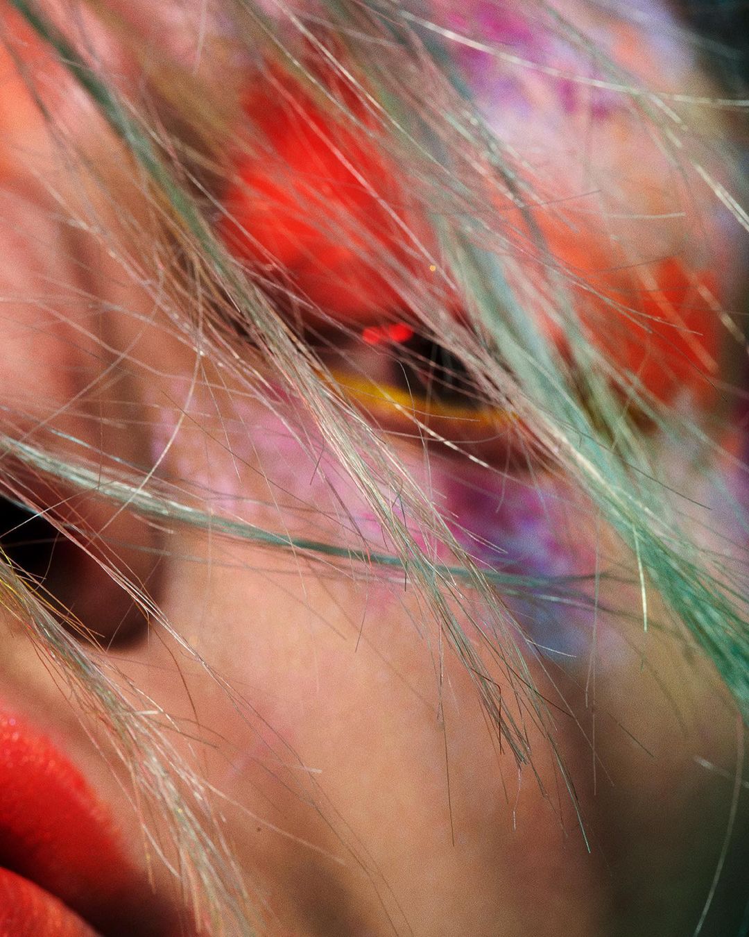 Macro shot of a face with pastel hair and vibrant red, yellow, and pink makeup, creating an artistic and colorful close-up.