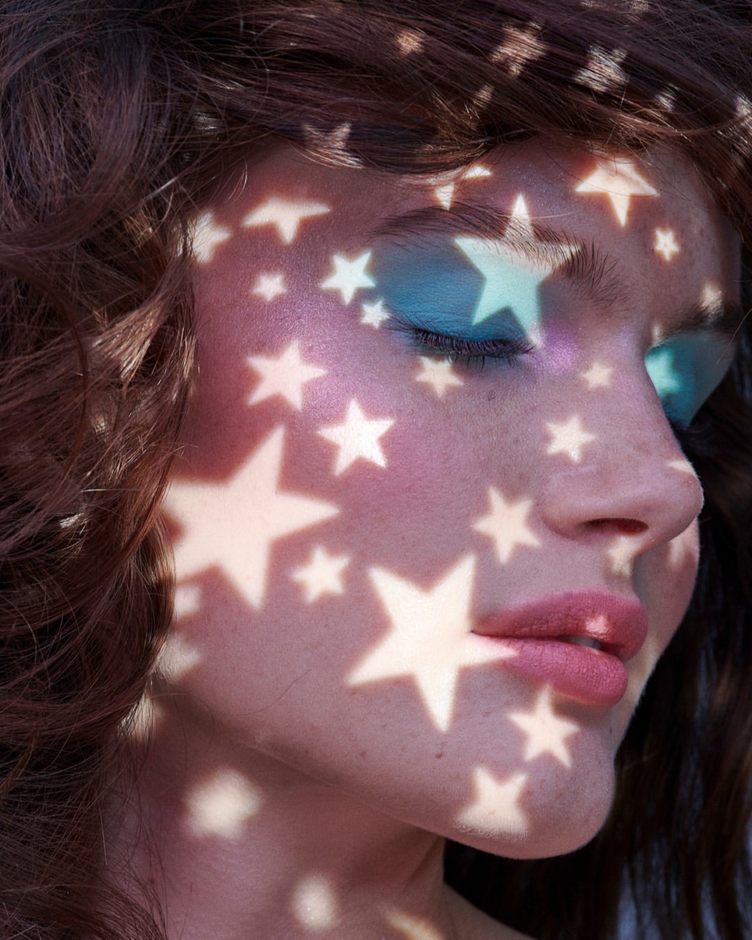 Close-up portrait of a woman with star-shaped shadows and bright blue eyeshadow for a beauty or fashion campaign.