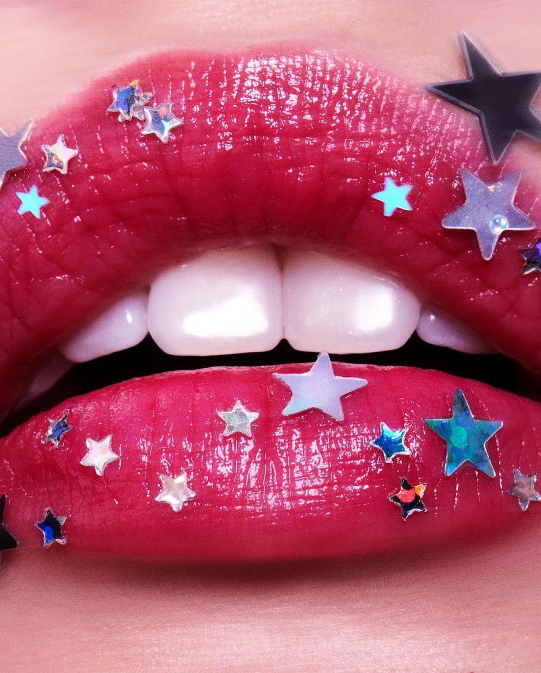 Close-up of glossy red lips with white teeth showing, adorned with star-shaped glitter. Beauty shot, fashion, studio lighting.
