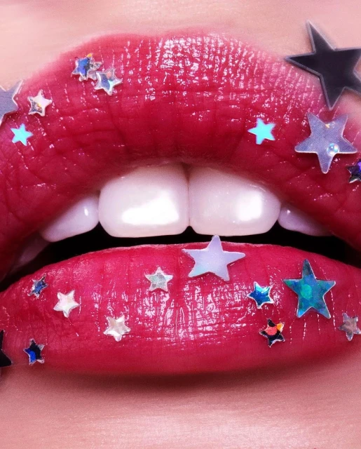 Close-up of glossy red lips with white teeth showing, adorned with star-shaped glitter. Beauty shot, fashion, studio lighting.