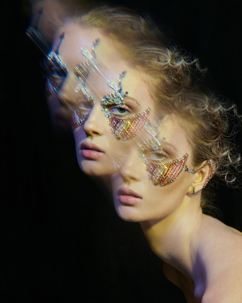 Close-up of a woman with face jewelry and soft light, posing in front of a dark background, creating a beauty and fashion portrait.