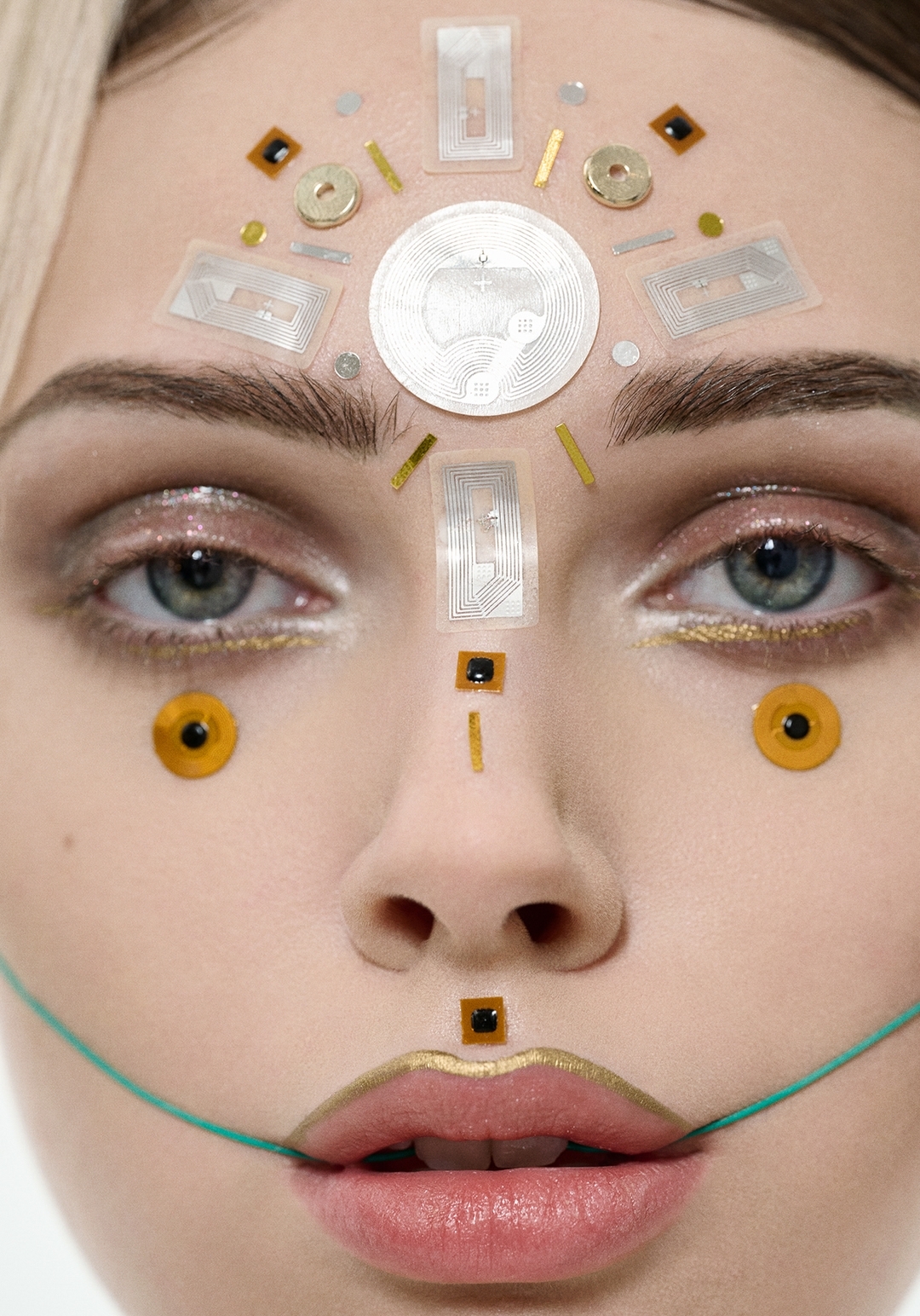 Close-up portrait of a woman with artful makeup and metallic ornamentation; a futuristic beauty concept in a studio setting.