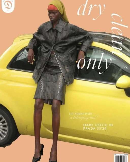 Fashion editorial shot of a Black female model in a jacket and skirt leaning against a yellow car, styled with a headscarf and high heels.
