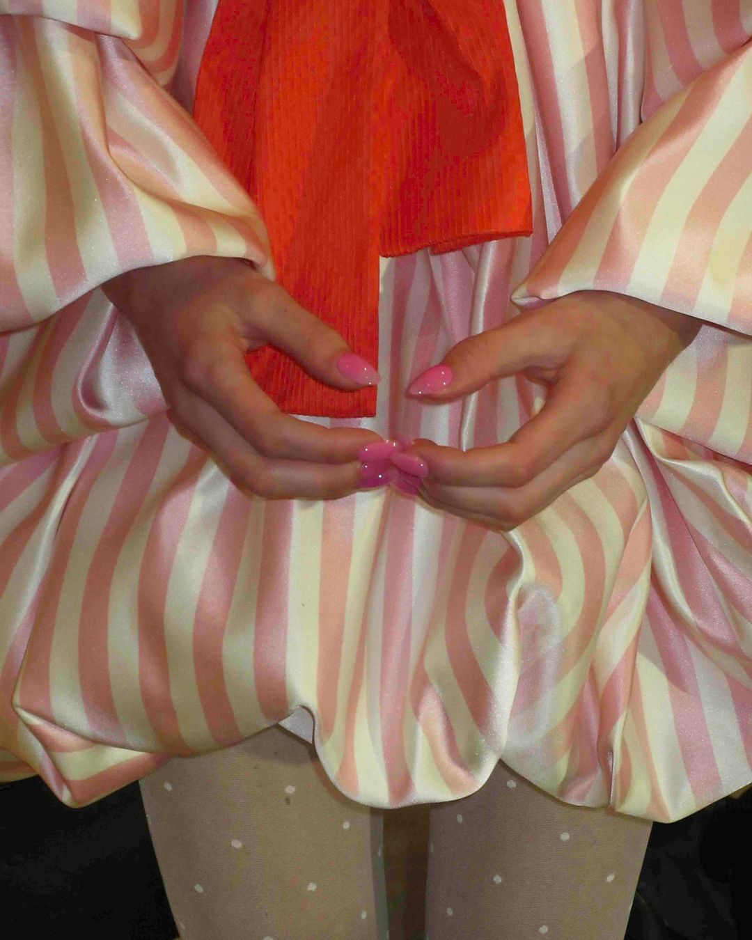 Close-up shot of a person wearing a striped dress with an orange sash, paired with polka dot tights, showcasing a fashion-forward look.