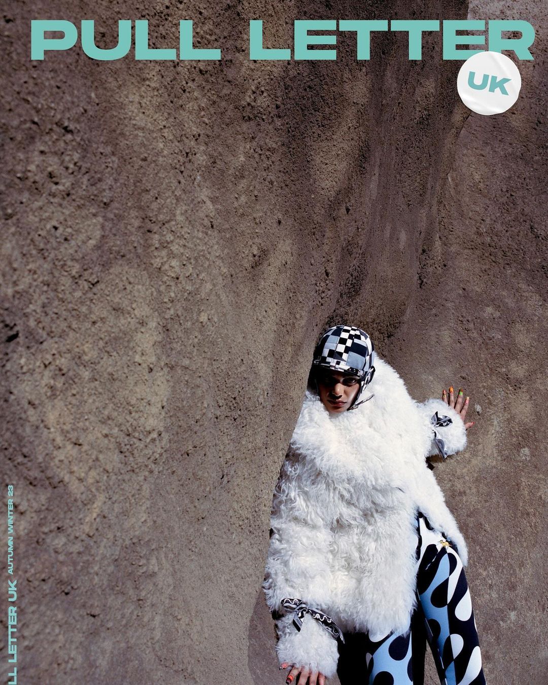 Fashion magazine cover featuring a stylish adult female model wearing a faux fur coat and patterned pants posing against a stone wall.