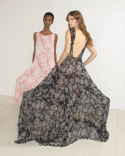 Two fashion models pose in flowing floral-print dresses against a white background in a studio setting, showcasing elegant and airy designs.