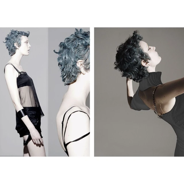 Fashionable young woman with blue hair in black outfit poses in a studio, showcasing a modern and edgy style against a grey background.