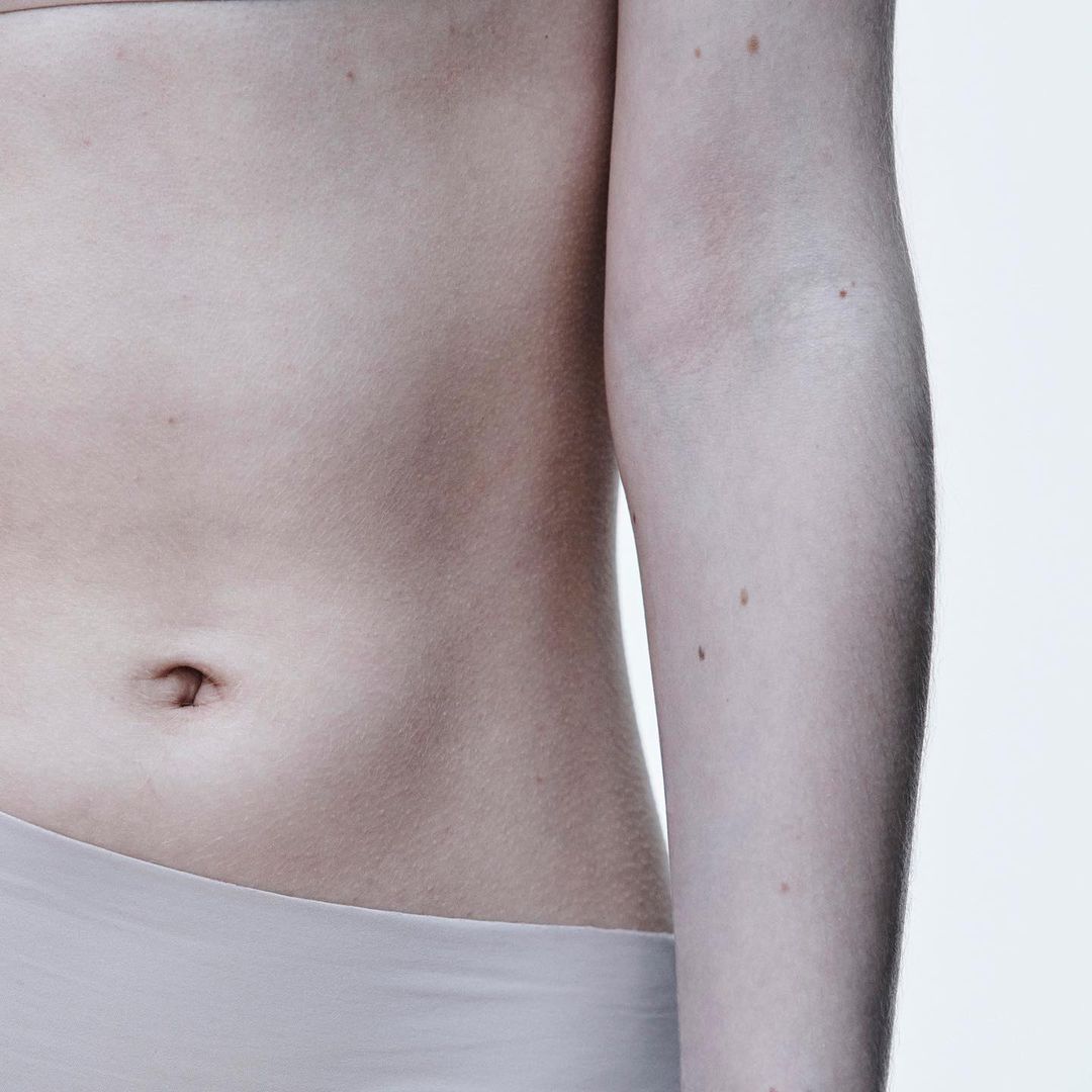 Close-up of a fair-skinned person's torso showing the abdomen, arm, and waist against a bright white backdrop in a clean studio shot.
