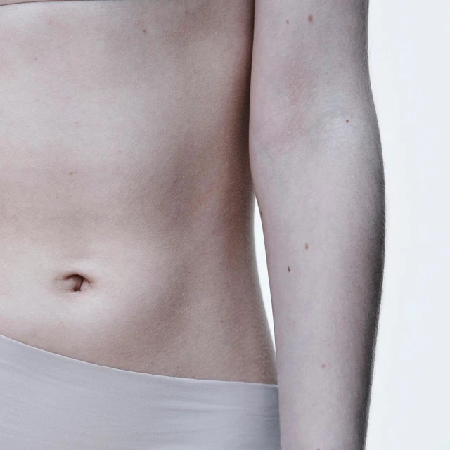 Close-up of a fair-skinned person's torso showing the abdomen, arm, and waist against a bright white backdrop in a clean studio shot.