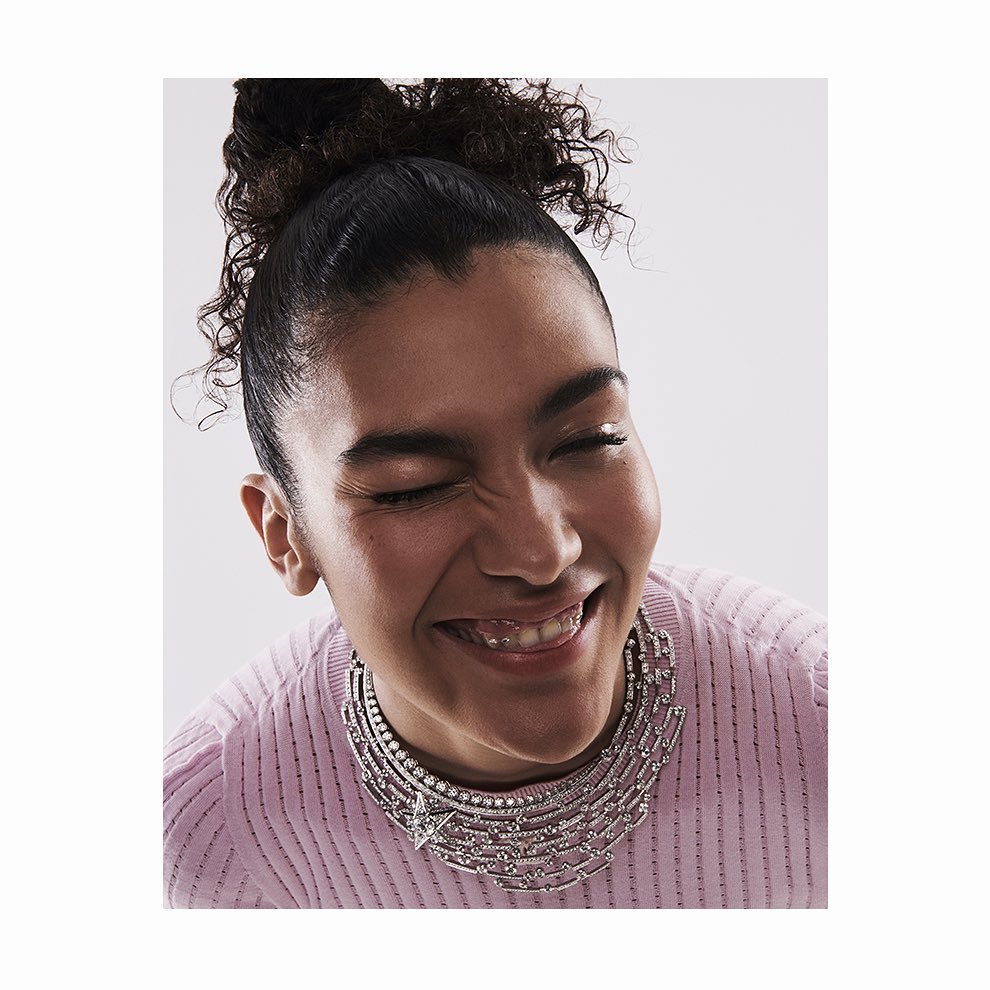 Smiling woman in pink sweater with a layered silver statement necklace against a white backdrop in a close-up shot.