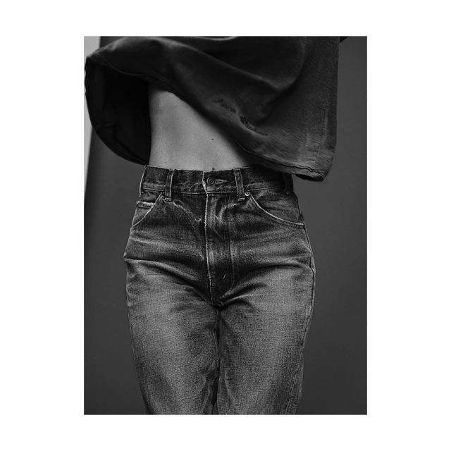 Black and white studio shot of adult woman's torso and jeans, low rise, with dark top partially concealing upper body and stomach.