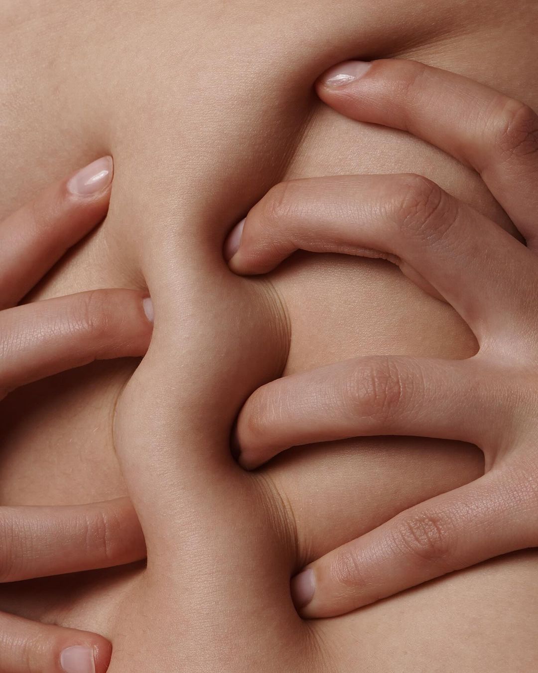 Close-up of fair skin being pinched by multiple hands creating textured folds of flesh with natural lighting and neutral color palette.