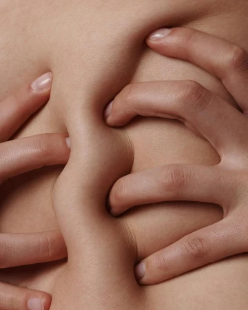 Close-up of fair skin being pinched by multiple hands creating textured folds of flesh with natural lighting and neutral color palette.