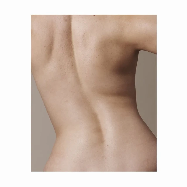 Close-up of a woman's back showing skin texture and musculature against a neutral background in a vertical studio shot.