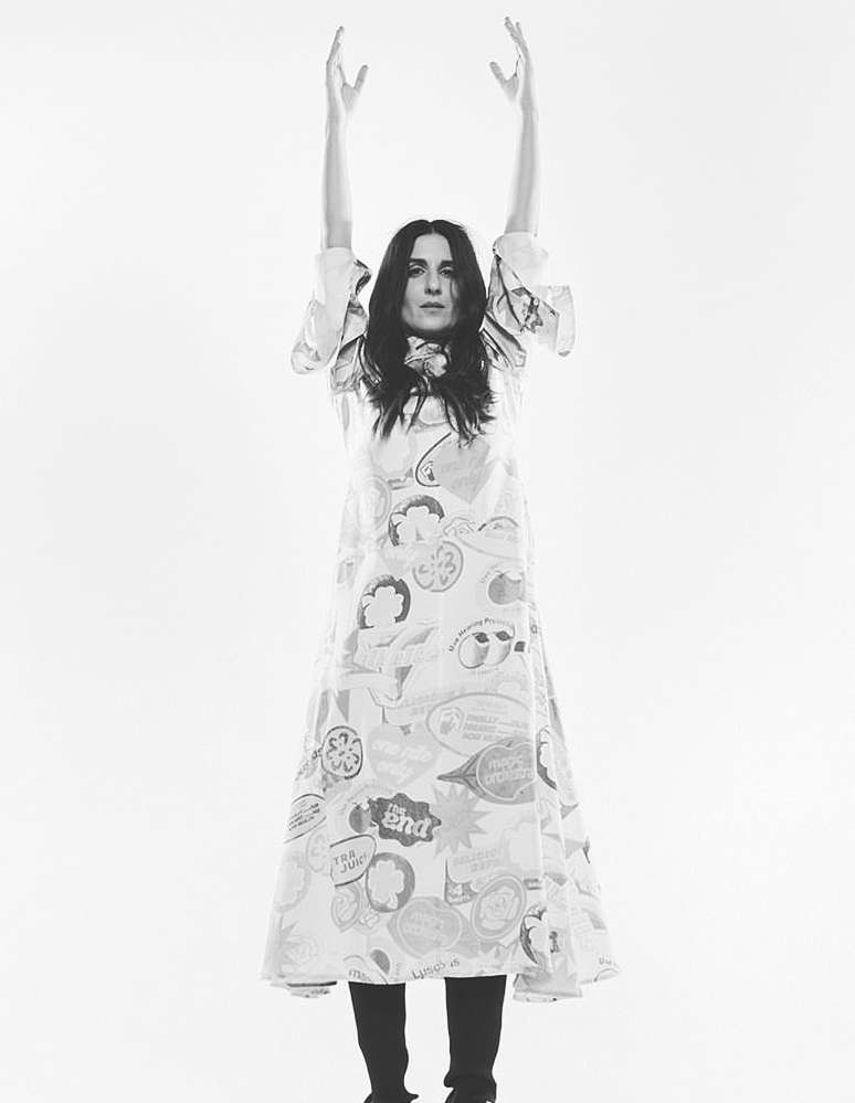 Black and white studio shot of a woman in a printed dress raising her arms against a white background, fashion portrait.