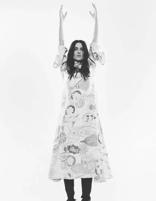 Black and white studio shot of a woman in a printed dress raising her arms against a white background, fashion portrait.