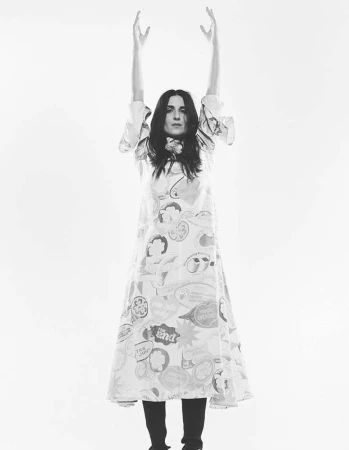 Black and white studio shot of a woman in a printed dress raising her arms against a white background, fashion portrait.
