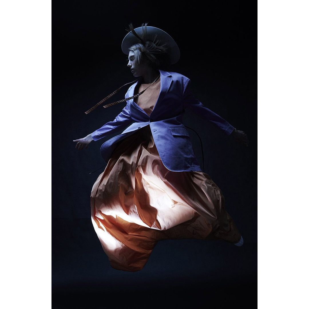 Fashionable woman with a hat and blue blazer levitates in a dramatic studio shot. Modern, bold and feminine fashion.