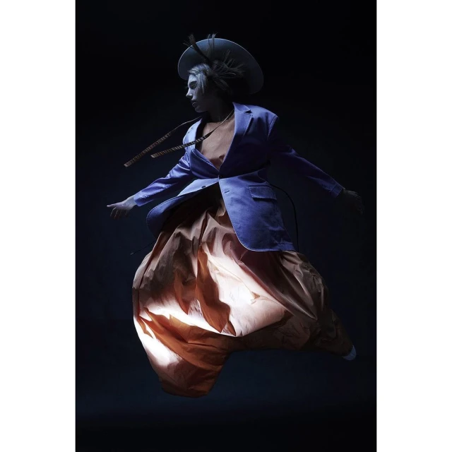Fashionable woman with a hat and blue blazer levitates in a dramatic studio shot. Modern, bold and feminine fashion. 