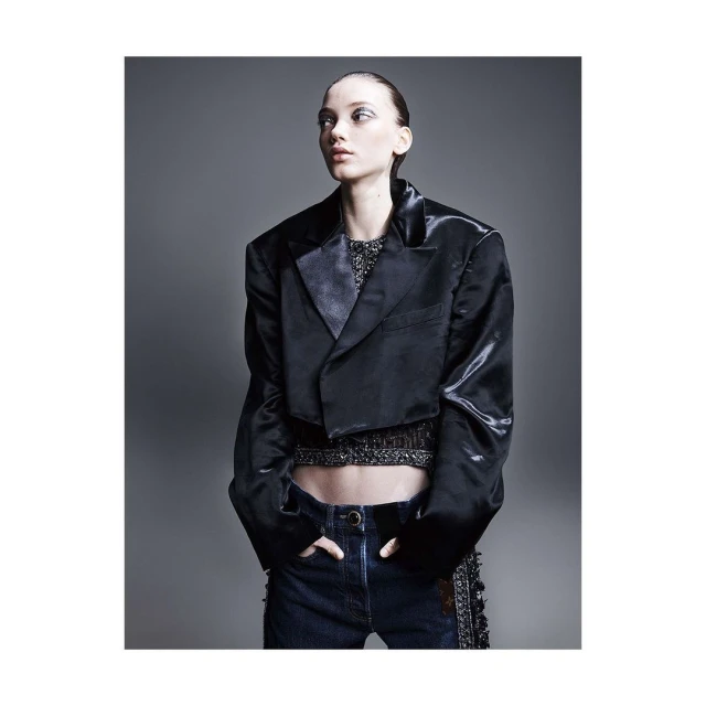 Fashion shot of a model in a dark jacket and jeans, posing in a photo studio with grey backdrop. The model is looking off to the side.