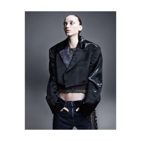 Fashion shot of a model in a dark jacket and jeans, posing in a photo studio with grey backdrop. The model is looking off to the side.