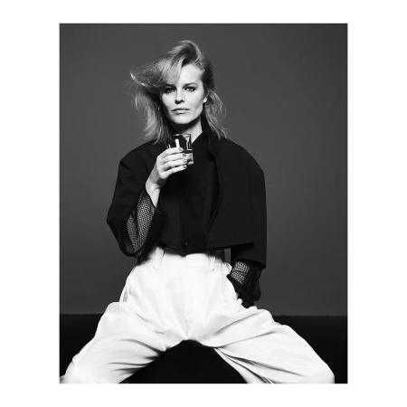 Black and white portrait of an adult female in a black blazer and white pants holding a glass, posing in a photo studio.