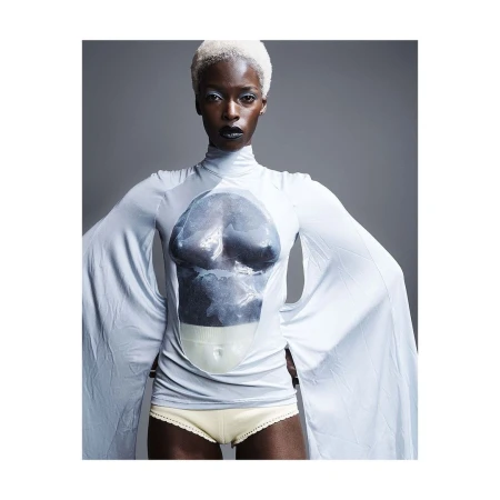 Striking studio portrait of a black female fashion model with white hair wearing a light blue long-sleeve top against gray backdrop.