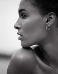 Close-up black and white profile portrait of a woman resting her chin on her shoulder, wearing small hoop earrings.
