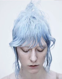 Close-up portrait of a woman with pastel blue dyed hair and closed eyes against a white background.
