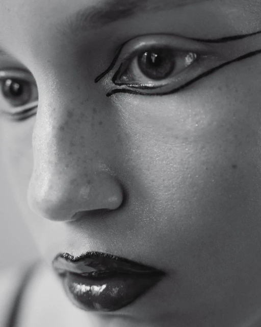 Close-up black and white portrait of a person's face featuring glossy dark lipstick and distinct black graphic eyeliner.