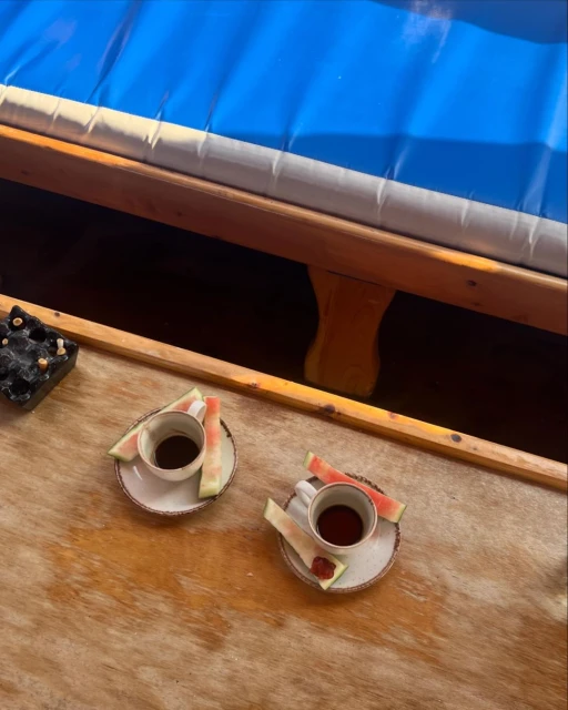 Two cups of dark liquid with watermelon slices on a rustic table, set against a blurred blue background, creating a cozy, summery vibe.