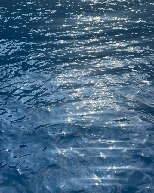 Sparkling turquoise water with gentle ripples and sun reflections creating a dynamic, textured surface, reminiscent of a serene ocean scene.