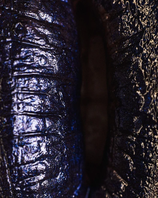 Close-up of a glossy, textured surface with alternating ridges and smooth areas, showcasing dark blue and black hues and light reflections.