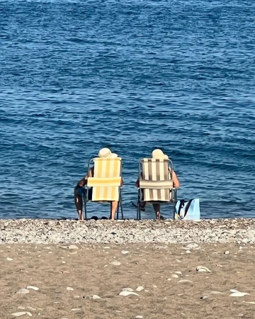 Two people sitting on beach chairs by the ocean with a dog and a tote bag on a sunny day, enjoying the coastal scenery.
