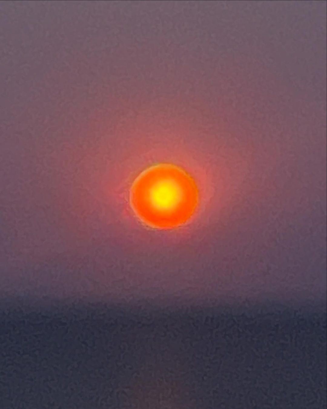 Vibrant orange sun during sunset or sunrise over a calm body of water with a pink and purple gradient sky, no visible people.