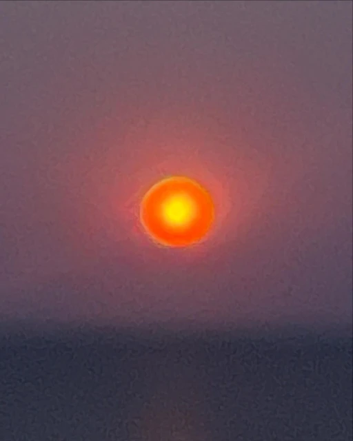 Vibrant orange sun during sunset or sunrise over a calm body of water with a pink and purple gradient sky, no visible people.