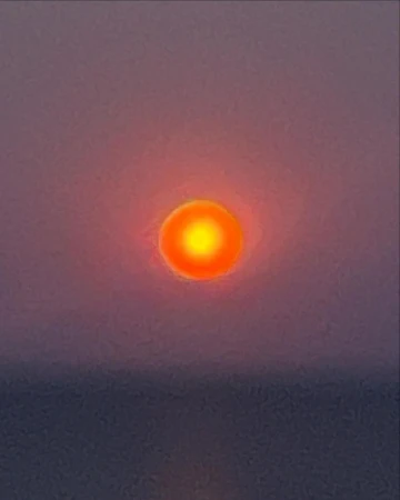 Vibrant orange sun during sunset or sunrise over a calm body of water with a pink and purple gradient sky, no visible people.
