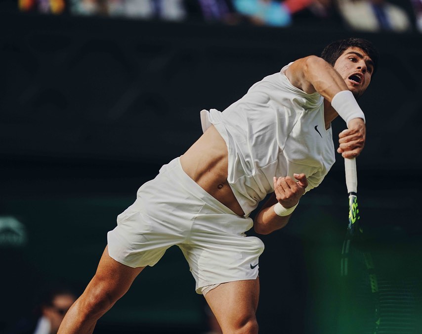 Male tennis player in action serving the ball during a match on outdoor tennis court in bright daylight, wearing sportswear.