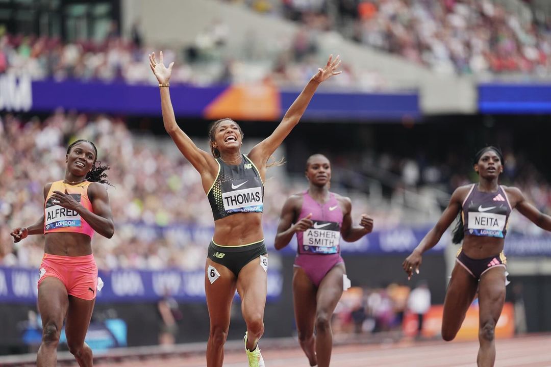 Female athlete, wearing number 6, crosses the finish line with arms raised in victory, followed closely by three other runners.
