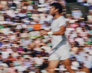 Motion blurred action shot of a tennis player in white holding a racket against a crowded stadium spectator backdrop