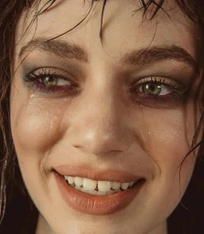 Close-up portrait of a woman with wet hair, tear streaks on her face, green eyes, and a slight smile, photographed by Janell Shirtcliff.