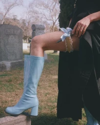 Close-up of a person in a black dress wearing light blue go-go boots and a garter with a blue bow in a cemetery