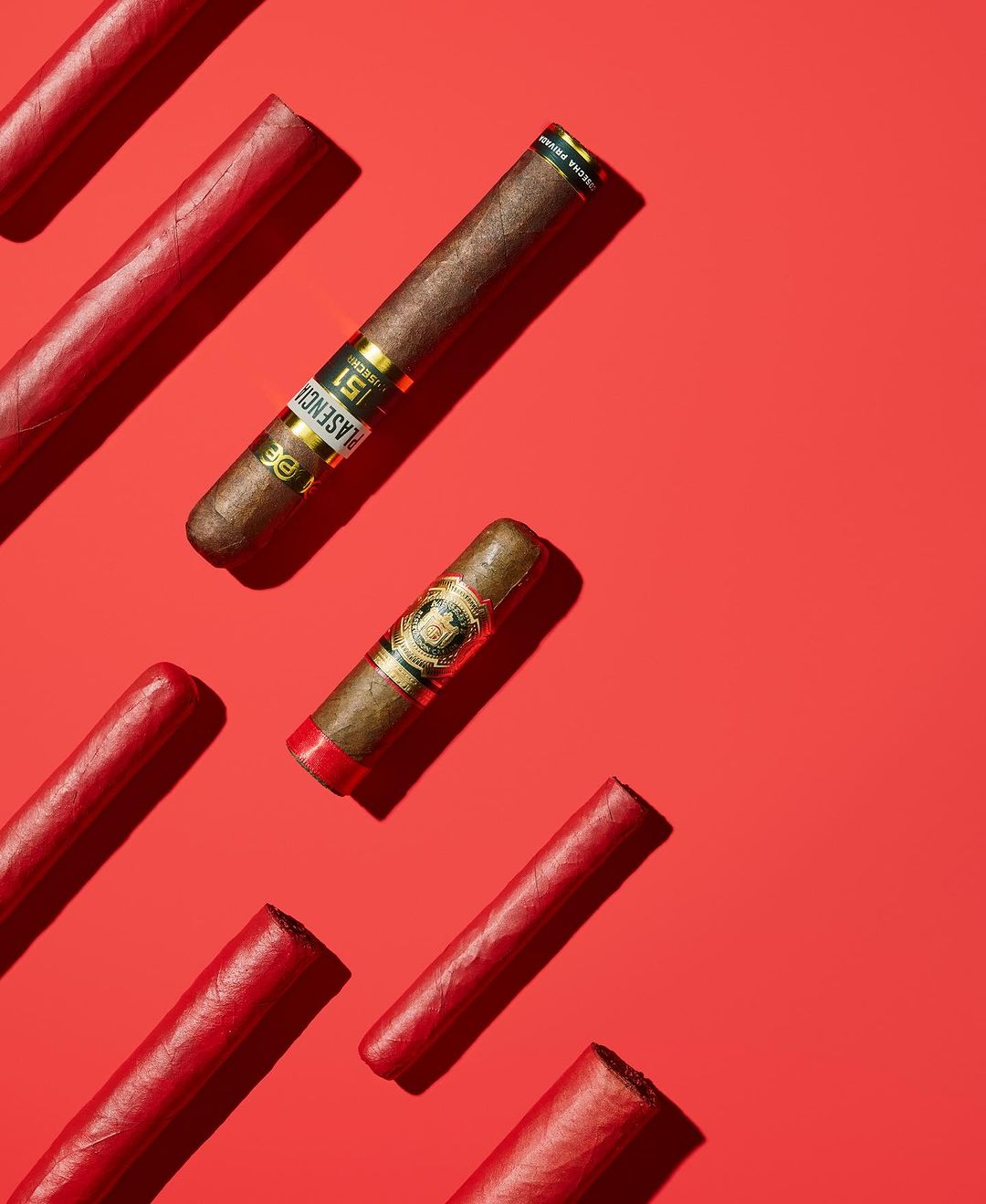 Still life photograph featuring several cigars and cigarillos against a vibrant red backdrop, showcasing varied sizes and textures.