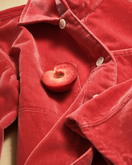 Close-up of a sliced plum placed on a folded, red velvet jacket with white buttons, creating a luxurious, textured, and minimalist composition.