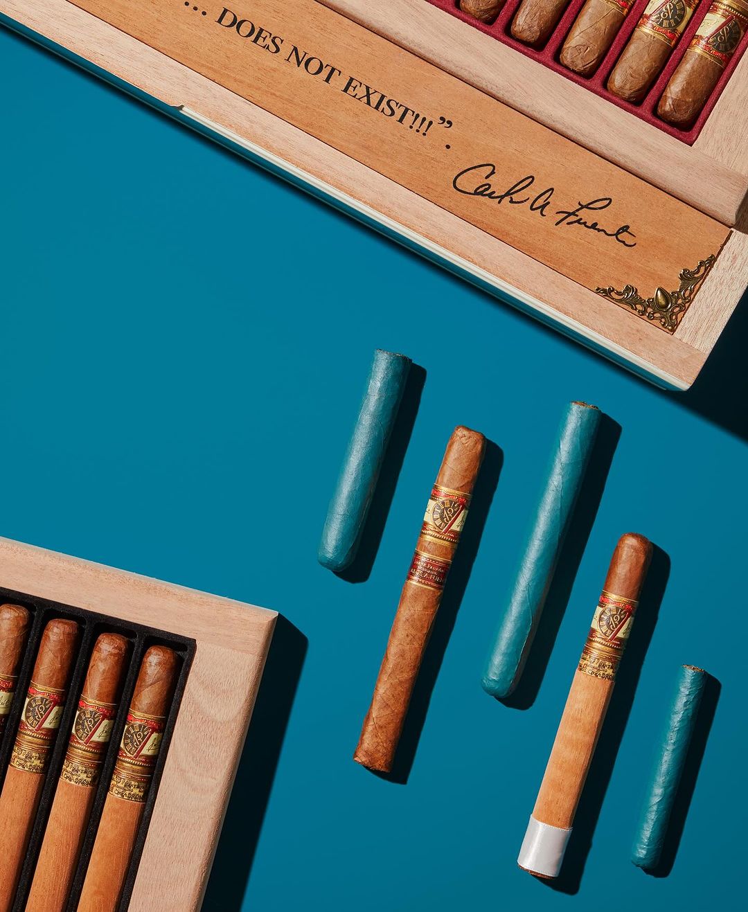 Overhead shot of premium cigars in wood boxes and individual cigar cases arranged on a teal background with clean studio lighting.