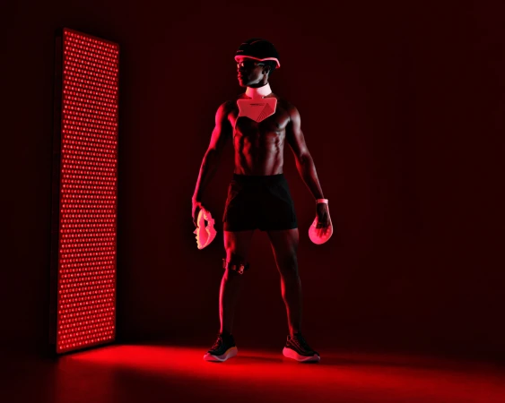 A Black man stands in profile wearing a futuristic helmet and chest plate, illuminated by a tall, glowing red LED therapy panel.