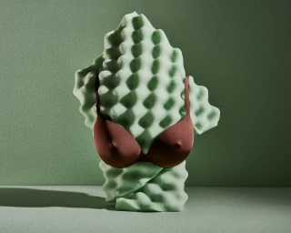 A brown satin bra displayed on a jagged, pale green acoustic foam block against a matching green background