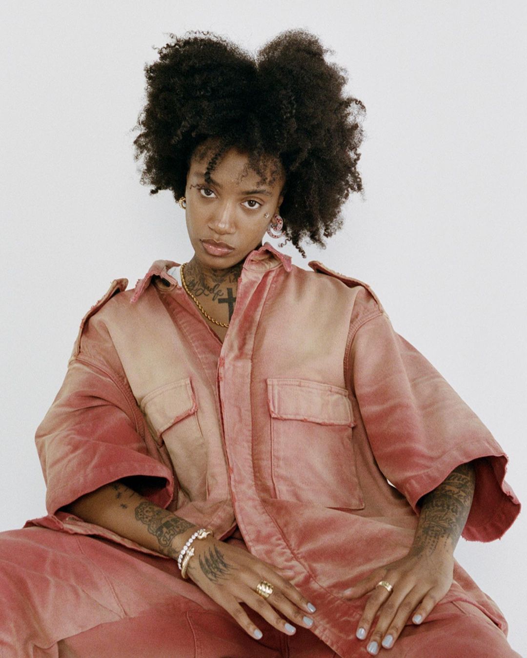 Woman with afro wearing oversized jumpsuit. Portrait of a cool young woman in loose fitting pink apparel against a white backdrop.