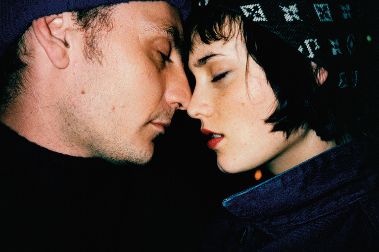 Close-up shot of a romantic couple. A fair-skinned man in a dark beanie with stubble touches noses with a fair-skinned woman.